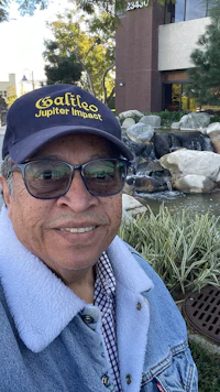 a man wearing a denim jacket and a hat in front of a fountain